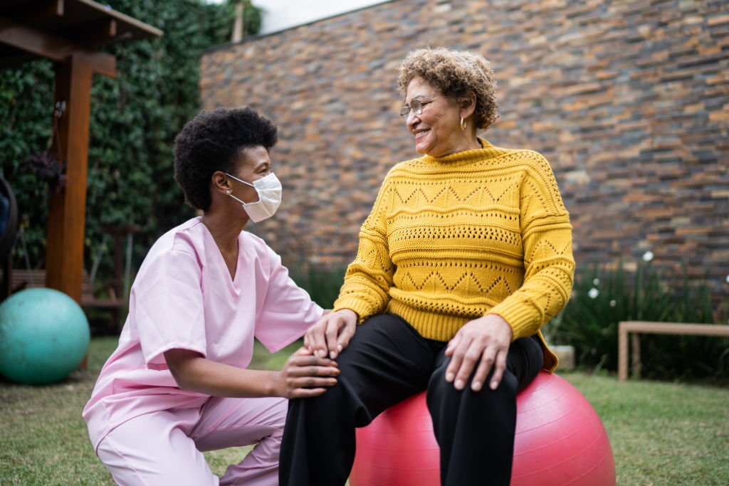 Nurse with senior patient doing exercise at home - using protective face mask