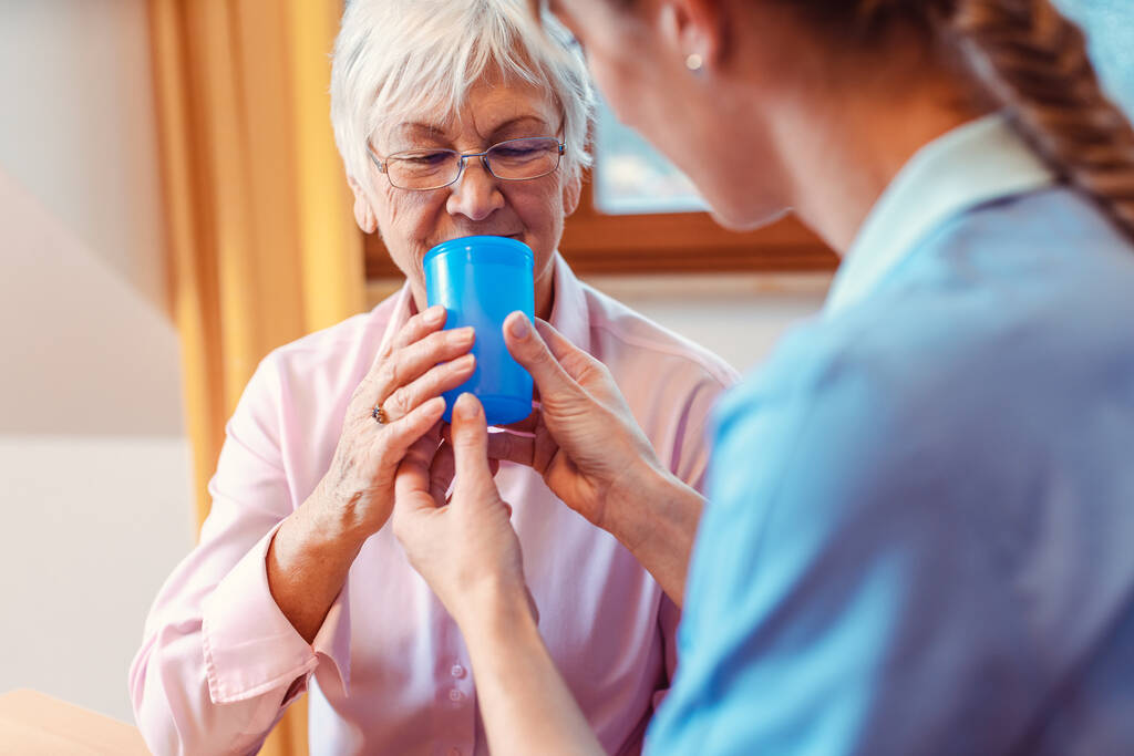 Caregiver helping senior woman drinking giving her a cup of water